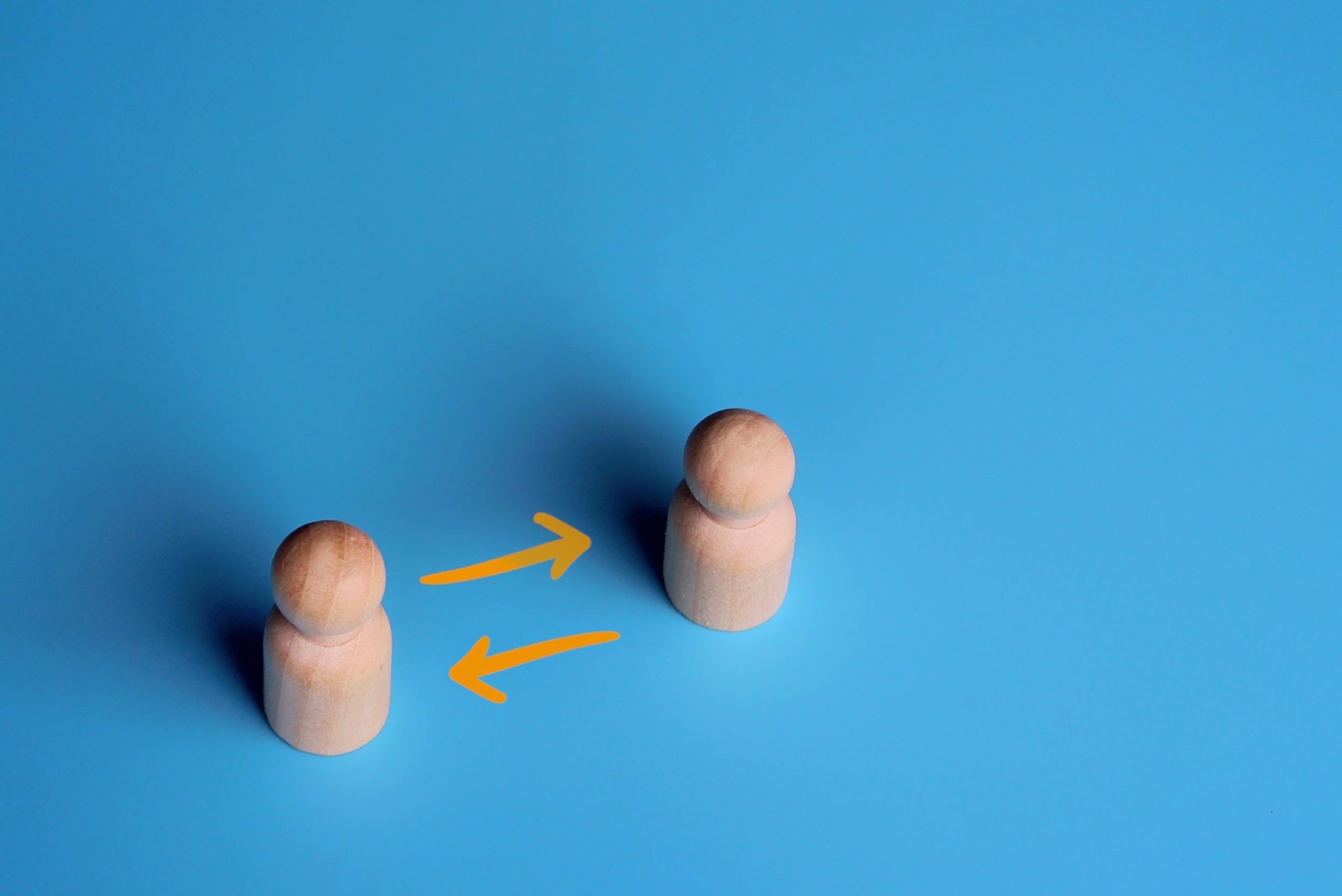 Wooden dolls and exchange arrow on blue background. Copy space.