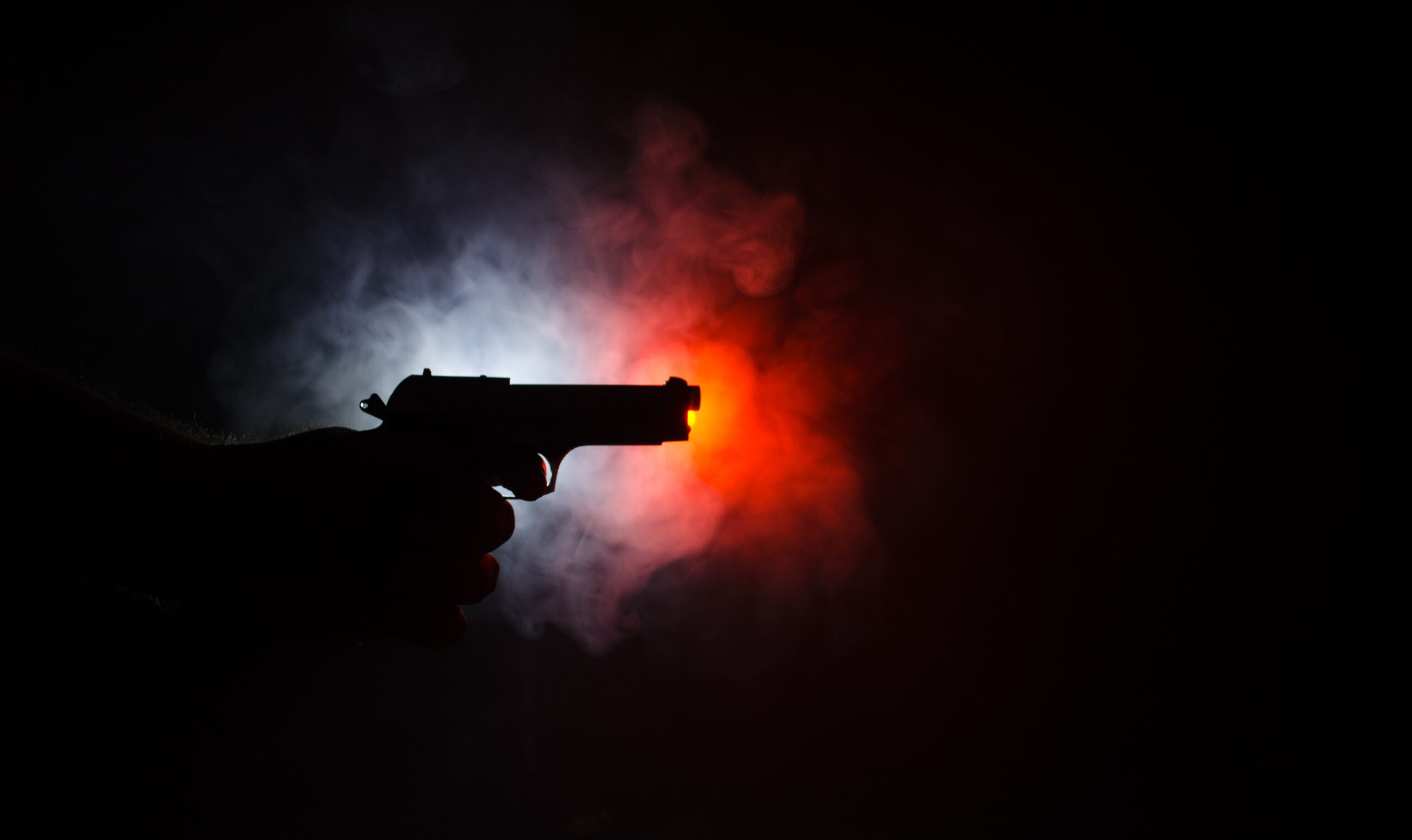 Male hand holding gun on black background with smoke ( yellow orange red white ) colored back lights,